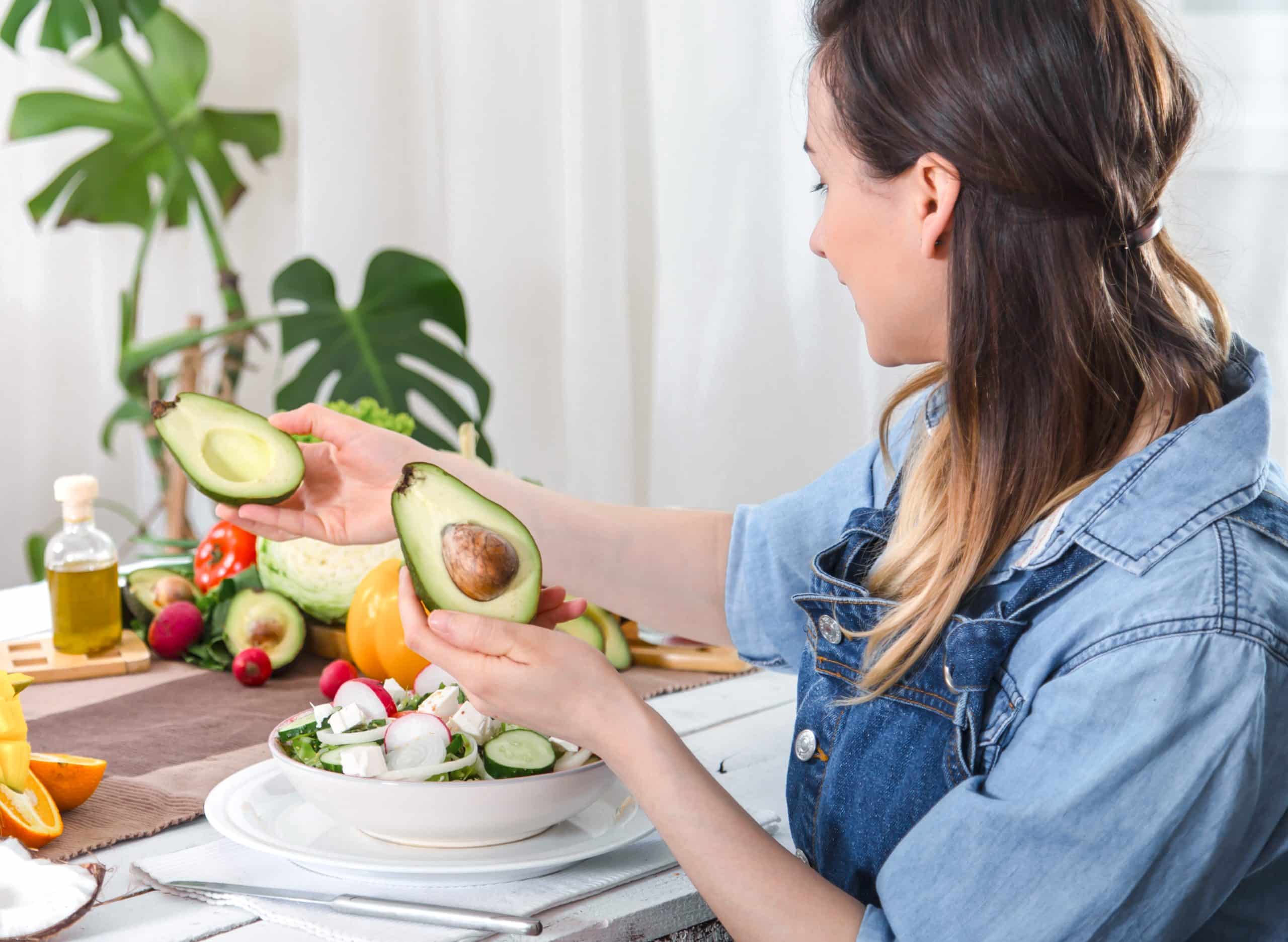 Young and happy woman eating salad with organic vegetables at the table on a light background , in denim clothes. The concept of a healthy home-made food.